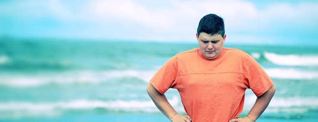 Man in an orange shirt standing beside the sea