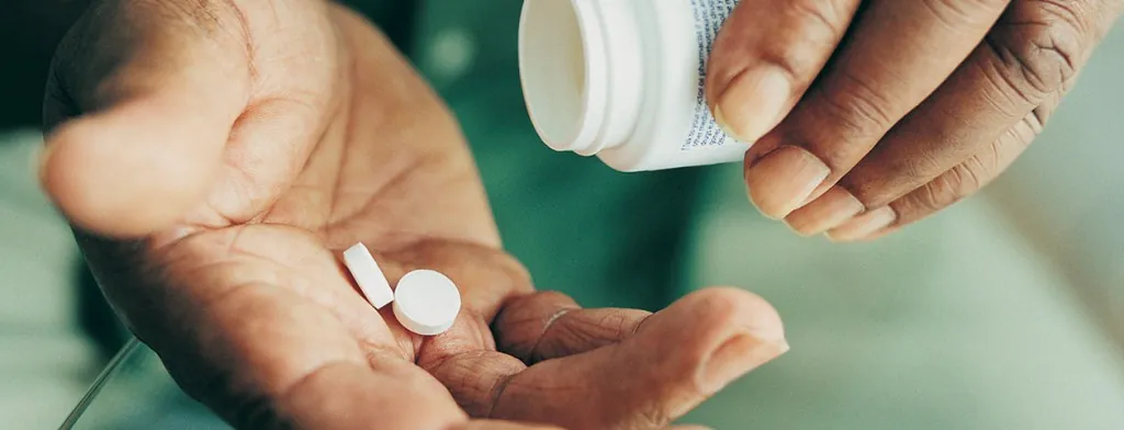 Person tipping tablets from a bottle into a hand