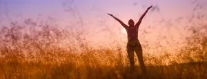 Person standing in a field with arms raised at sunset
