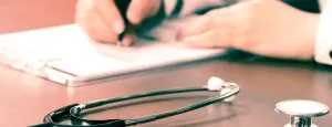 Person completing paperwork beside a stethoscope