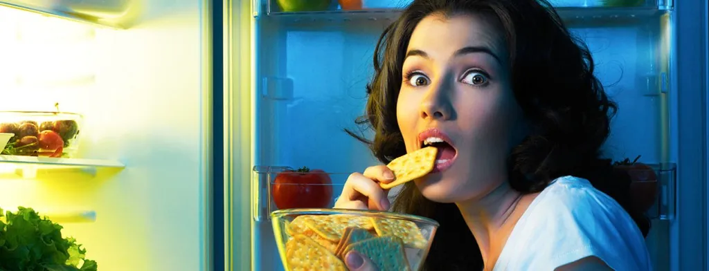 Woman eating beside an open refrigerator