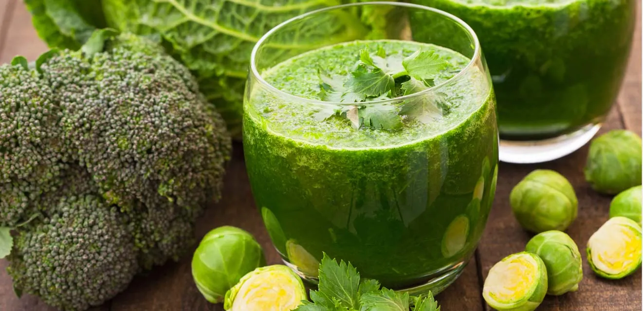 Green vegetable juice beside broccoli and Brussels sprouts