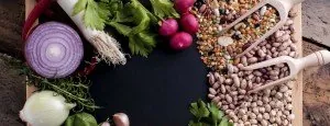 Fresh vegetables beside small bowls of grains and seeds
