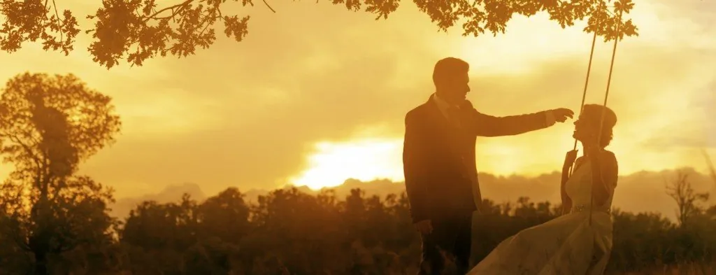 Person pushing another person on a swing at sunset