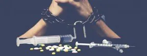 Person seated at a table with pills and other drug paraphernalia