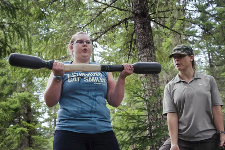 Woman exercising with a weighted bar outdoors while a coach watches