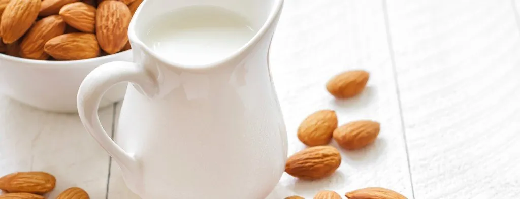 Milk being poured into a cup beside almonds