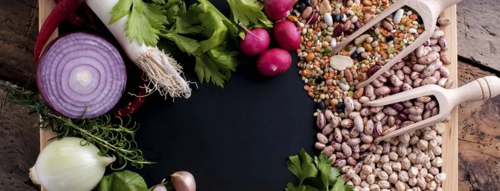 Fresh vegetables beside small bowls of grains and seeds