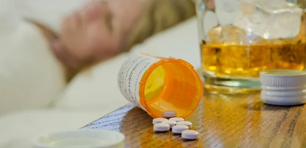 Medicine bottle and glass beside a person lying down