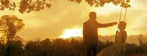 Person pushing another person on a swing at sunset