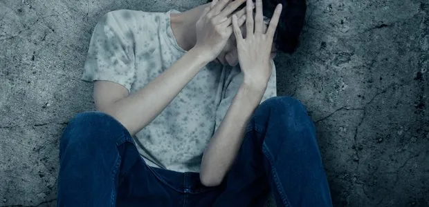 Person sitting against a wall with hands raised near their face