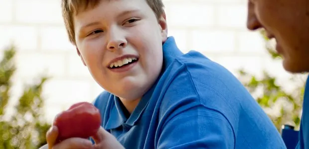 Child holding an apple while talking with an adult