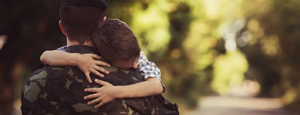 Person in military uniform embracing a child