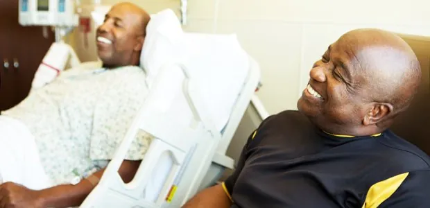 Person lying in a hospital bed with a visitor nearby