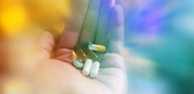 Hand holding several tablets and capsules